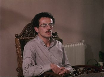 Movie still from “Close-Up” (1990), directed by Abbas Kiarostami – A man sitting in a wooden chair wearing glasses; Medium shot, Low angle