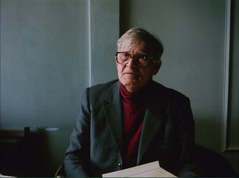 Movie still from “Close-Up” (1990), directed by Abbas Kiarostami – An older man sitting at a table in front of a window; Close Up shot, Over the shoulder angle