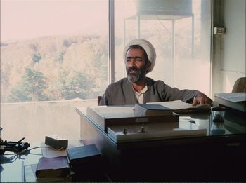 Movie still from “Close-Up” (1990), directed by Abbas Kiarostami – An older man sitting at a desk in front of a window; Medium shot, Low angle