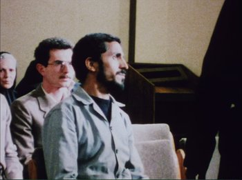 Movie still from “Close-Up” (1990), directed by Abbas Kiarostami – A man sitting in front of another man in front of a microphone; Medium shot, Over the shoulder angle