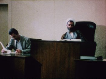 Movie still from “Close-Up” (1990), directed by Abbas Kiarostami – Two men sitting at a table in a courtroom; Medium shot, High angle