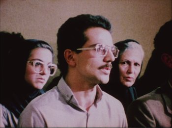 Movie still from “Close-Up” (1990), directed by Abbas Kiarostami – A group of people standing next to each other wearing glasses; Close Up shot, Low angle