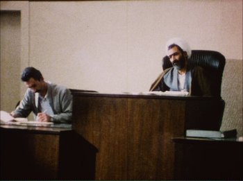 Movie still from “Close-Up” (1990), directed by Abbas Kiarostami – Two men sitting at a table in a courtroom; Medium shot, Low angle