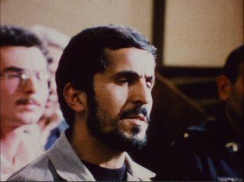 Movie still from “Close-Up” (1990), directed by Abbas Kiarostami – A person with a beard looking at something; Close Up shot, Over the shoulder angle