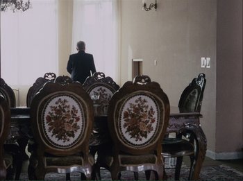 Movie still from “Close-Up” (1990), directed by Abbas Kiarostami – A man sitting at a dining room table; Wide shot, Over the shoulder angle