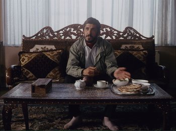 Movie still from “Close-Up” (1990), directed by Abbas Kiarostami – A man sitting at a table with a tray of food; Medium shot, High angle
