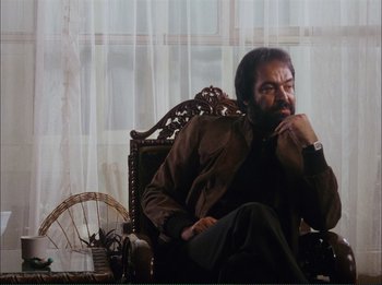 Movie still from “Close-Up” (1990), directed by Abbas Kiarostami – A man sitting in a chair in front of a window; Medium shot, Low angle