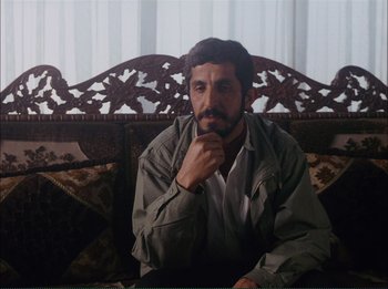Movie still from “Close-Up” (1990), directed by Abbas Kiarostami – A man sitting on top of a wooden bench; Medium shot, Over the shoulder angle