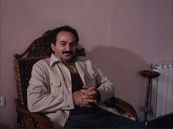 Movie still from “Close-Up” (1990), directed by Abbas Kiarostami – A man sitting in a chair with his hands crossed; Medium shot, High angle