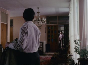 Movie still from “Close-Up” (1990), directed by Abbas Kiarostami – A man standing in front of an open door looking at another man; Wide shot, Over the shoulder angle