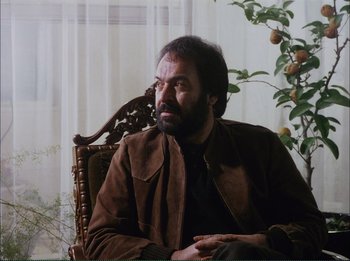 Movie still from “Close-Up” (1990), directed by Abbas Kiarostami – A man sitting in a chair in front of a window; Medium shot, Low angle