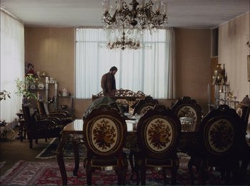 Movie still from “Close-Up” (1990), directed by Abbas Kiarostami – A man standing in front of a dining room table; Wide shot, High angle