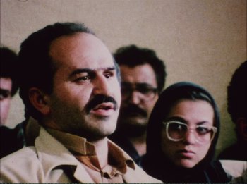 Movie still from “Close-Up” (1990), directed by Abbas Kiarostami – A man and a woman standing next to another man; Close Up shot, Low angle