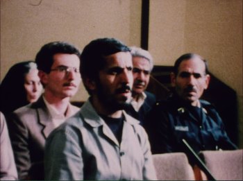 Movie still from “Close-Up” (1990), directed by Abbas Kiarostami – A group of men sitting next to each other in front of a microphone; Medium shot, Over the shoulder angle