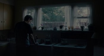 Movie still from “Closet Monster” (2015), directed by Stephen Dunn – A man standing in front of a kitchen sink; Medium shot, Over the shoulder angle