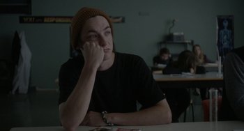 Movie still from “Closet Monster” (2015), directed by Stephen Dunn – A man sitting at a table in front of a book; Close Up shot, Over the shoulder angle