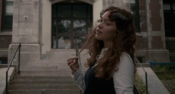 Movie still from “Closet Monster” (2015), directed by Stephen Dunn – A young woman with long curly red hair holding an umbrella in front of a building; Medium shot, Over the shoulder angle