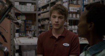 Movie still from “Closet Monster” (2015), directed by Stephen Dunn – A young man in a red shirt is in a store; Close Up shot, Over the shoulder angle