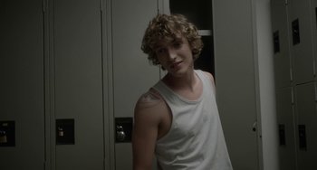 Movie still from “Closet Monster” (2015), directed by Stephen Dunn – A young man with a white tank top is posing for a picture; Medium shot, Over the shoulder angle