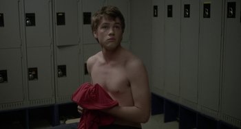 Movie still from “Closet Monster” (2015), directed by Stephen Dunn – A young man holding a red shirt in a locker room; Medium shot, Over the shoulder angle