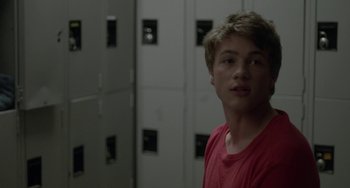 Movie still from “Closet Monster” (2015), directed by Stephen Dunn – A man in a red shirt standing in a room with lockers behind him; Close Up shot, Over the shoulder angle