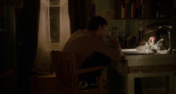 Movie still from “Closet Monster” (2015), directed by Stephen Dunn – A man sitting at a table in a room; Wide shot, High angle