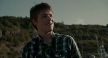 Movie still from “Closet Monster” (2015), directed by Stephen Dunn – A young man in a plaid shirt is smiling for the camera; Close Up shot, Over the shoulder angle