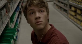 Movie still from “Closet Monster” (2015), directed by Stephen Dunn – A young man is listening intently to music while standing in a store; Close Up shot, High angle