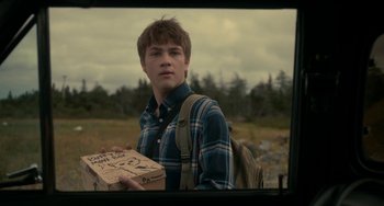 Movie still from “Closet Monster” (2015), directed by Stephen Dunn – A young man holding a cardboard box in a field; Close Up shot, Over the shoulder angle