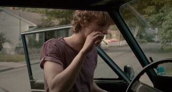 Movie still from “Closet Monster” (2015), directed by Stephen Dunn – A man smoking a cigarette while sitting in the driver's seat of a car; Medium shot, Over the shoulder angle