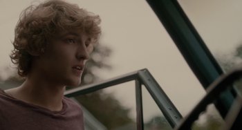 Movie still from “Closet Monster” (2015), directed by Stephen Dunn – A young man with curly blonde hair looking out a window; Close Up shot, Over the shoulder angle