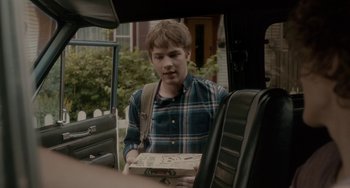 Movie still from “Closet Monster” (2015), directed by Stephen Dunn – A man in a plaid shirt holding a pizza box; Medium shot, Over the shoulder angle