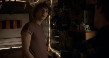 Movie still from “Closet Monster” (2015), directed by Stephen Dunn – A young man standing in a room with lights; Medium shot, Over the shoulder angle