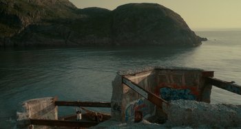Movie still from “Closet Monster” (2015), directed by Stephen Dunn – A man sitting on a dock next to a body of water; Extreme Wide shot, High angle