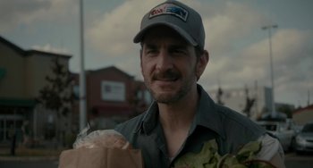 Movie still from “Closet Monster” (2015), directed by Stephen Dunn – A man wearing a hat and holding a paper bag; Close Up shot, Over the shoulder angle