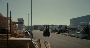 Movie still from “Closet Monster” (2015), directed by Stephen Dunn – A forklift driving down a street next to piles of lumber; Extreme Wide shot, Low angle