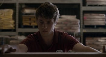 Movie still from “Closet Monster” (2015), directed by Stephen Dunn – A man sitting at a table looking at a computer screen; Medium shot, Over the shoulder angle