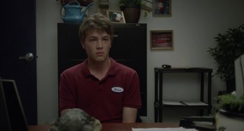Movie still from “Closet Monster” (2015), directed by Stephen Dunn – A man sitting at a table in front of a computer monitor; Medium shot, Over the shoulder angle