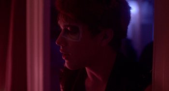 Movie still from “Closet Monster” (2015), directed by Stephen Dunn – A young man with makeup on his face looking out a window; Close Up shot, Over the shoulder angle