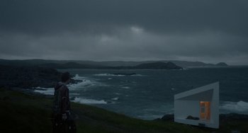 Movie still from “Closet Monster” (2015), directed by Stephen Dunn – A person standing on a hill near a body of water; Extreme Wide shot, Low angle