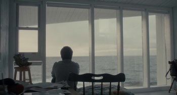 Movie still from “Closet Monster” (2015), directed by Stephen Dunn – A person sitting in front of a window looking out at the ocean; Wide shot, Over the shoulder angle