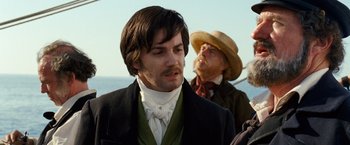 Movie still from “Cloud Atlas” (2012), directed by Lilly Wachowski – A man in a suit and a hat standing next to another man in a hat; Close Up shot, Over the shoulder angle