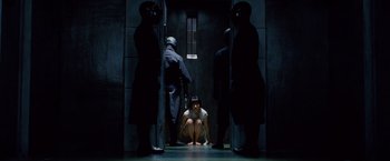 Movie still from “Cloud Atlas” (2012), directed by Lilly Wachowski – A group of men standing around a woman in a dark room; Wide shot, High angle