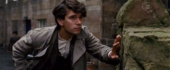 Movie still from “Cloud Atlas” (2012), directed by Lilly Wachowski – A man in a jacket and tie touching a wall; Close Up shot, Over the shoulder angle