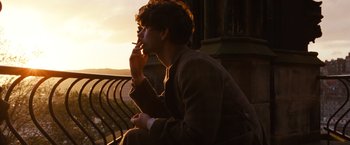 Movie still from “Cloud Atlas” (2012), directed by Lilly Wachowski – A man sitting on a railing smoking a cigarette at sunset; Medium shot, Over the shoulder angle