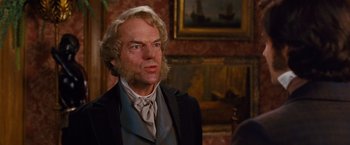Movie still from “Cloud Atlas” (2012), directed by Lilly Wachowski – A man with long blonde hair wearing a suit and tie; Close Up shot, Over the shoulder angle