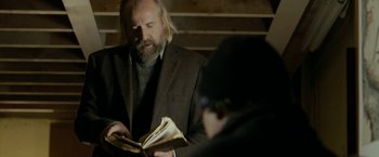 Movie still from “Clown” (2014), directed by Jon Watts – A man in a brown suit reading a book; Medium shot, Over the shoulder angle