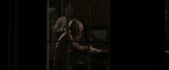 Movie still from “Clown” (2014), directed by Jon Watts – A little girl sitting at a kitchen table with an older man standing in the background; Medium shot, Over the shoulder angle