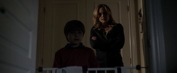 Movie still from “Clown” (2014), directed by Jon Watts – A woman and a boy standing next to each other in a dark room; Medium shot, Over the shoulder angle