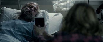 Movie still from “Clown” (2014), directed by Jon Watts – A man sitting in a hospital bed while holding a cell phone; Close Up shot, Over the shoulder angle